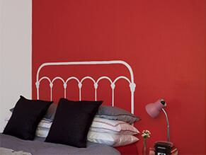 Bright red feature wall in kids bedroom with white and black pillows and lamp with grey bed sheets